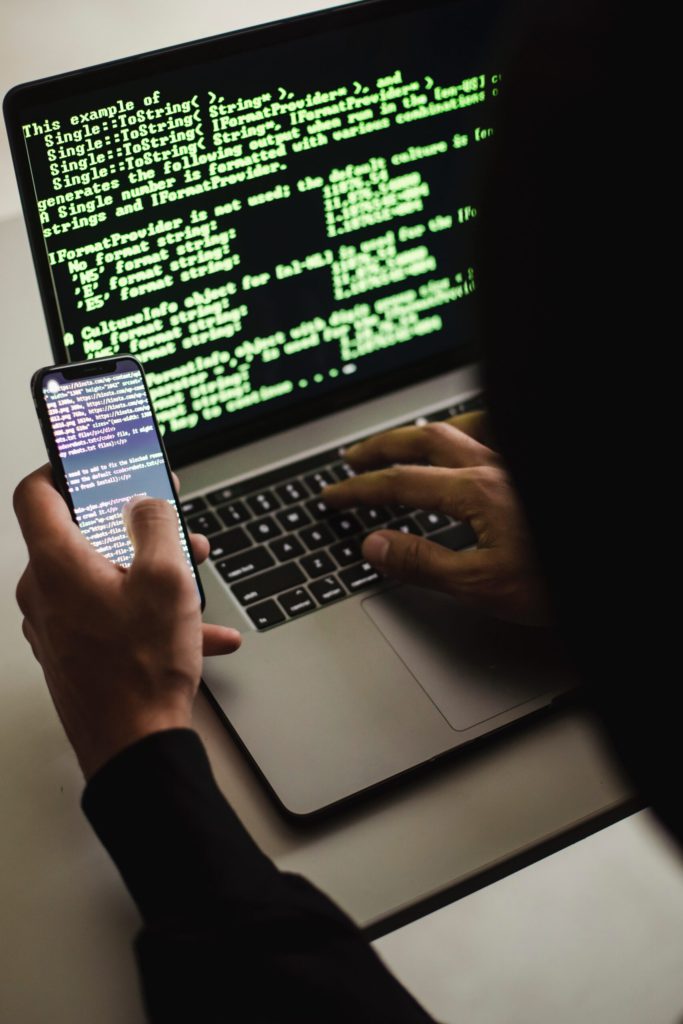 Free Unrecognizable hacker with smartphone typing on laptop at desk Stock Photo